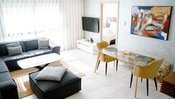 En moderne stue med sofa, sofabord og spisebord i glas med stole.