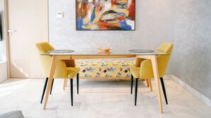 Et spiseområde med et glasbord, gule stole og en bordløber med blomstermønster.