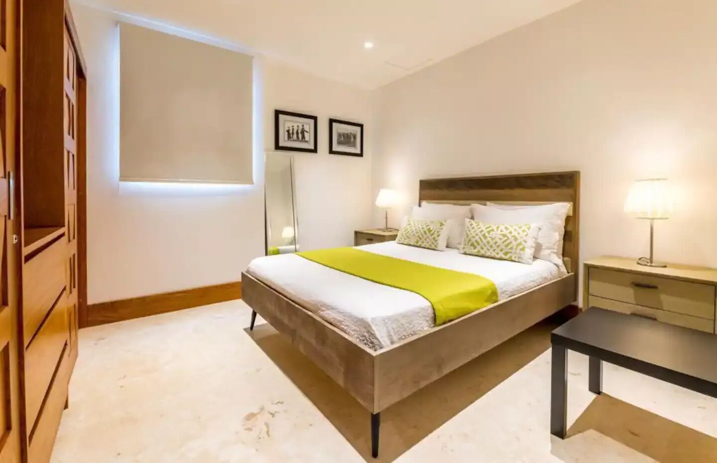Un dormitorio con cama, mesitas de noche, un tocador, un espejo y una ventana.