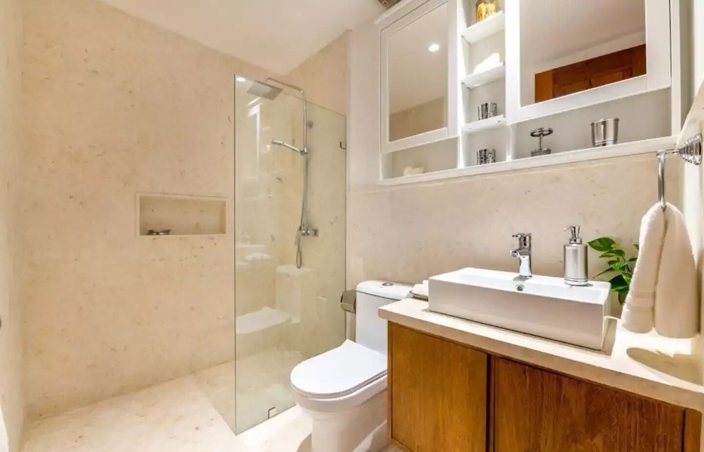 Een moderne badkamer met een douchecabine van glas, een toilet, een wastafel met spiegel erboven en houten kastjes.