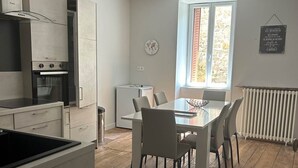 A modern kitchen with white cabinets, a built-in oven, and a dining area with a table and chairs. - The winged angels (MARCILLAC LA CROISILLE)