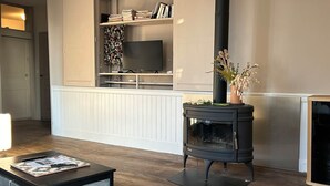 A living room with a black wood-burning stove, a television on a shelf, and a coffee table with a magazine. - The winged angels (MARCILLAC LA CROISILLE)