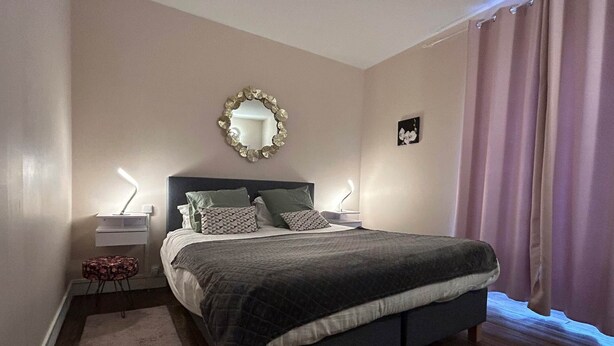 A bedroom with a bed, bedside lamps, a mirror, and a small table with a lamp.