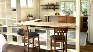 Une cuisine rustique avec des meubles en bois, une table à manger et des chaises. On y trouve des étagères remplies de vaisselle et une fenêtre qui laisse entrer la lumière naturelle.