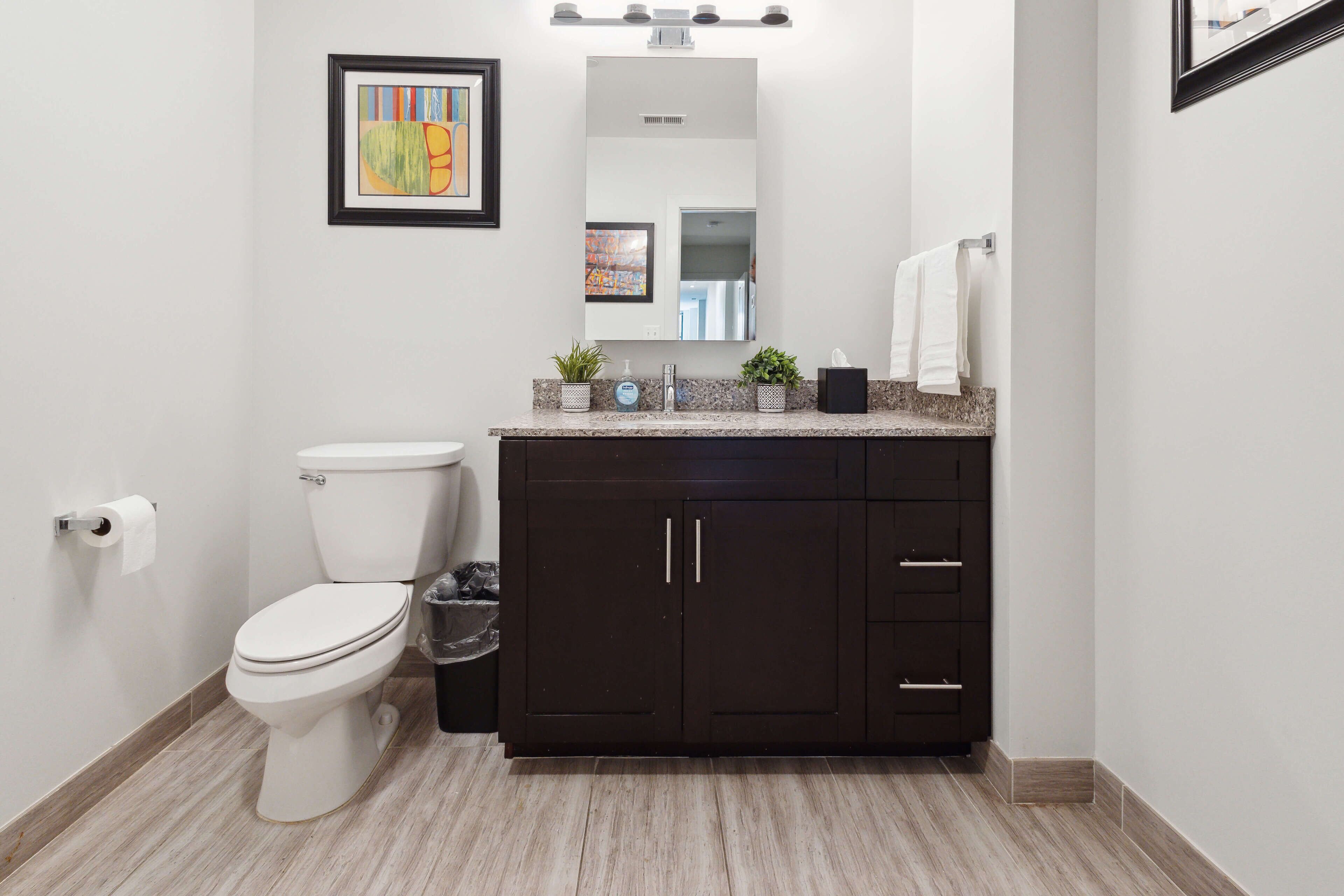 Un baño moderno con inodoro, muebles oscuros, un espejo y un lavabo con encimera.