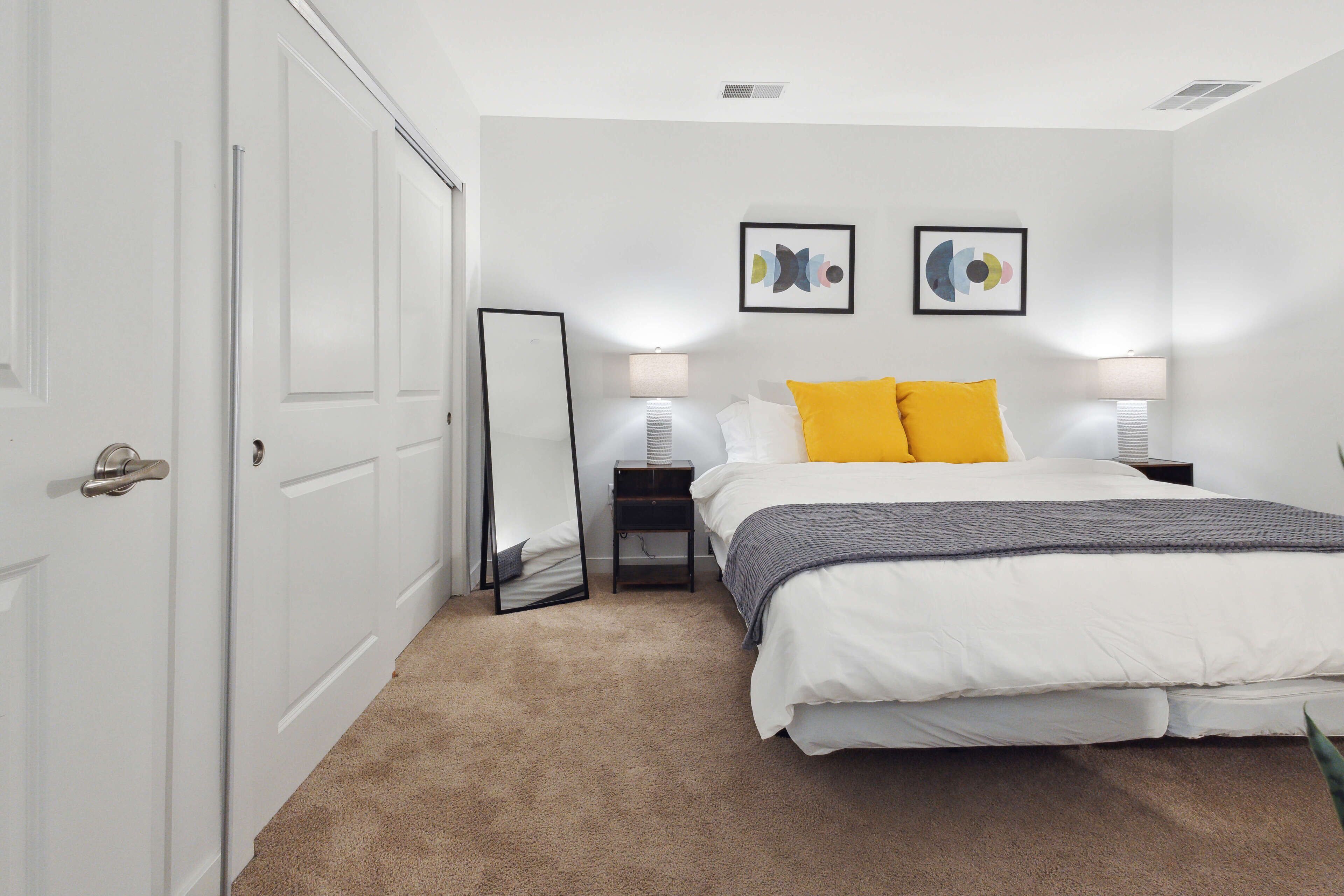 A bedroom with a bed, two bedside lamps, a mirror, and two wall art pieces.