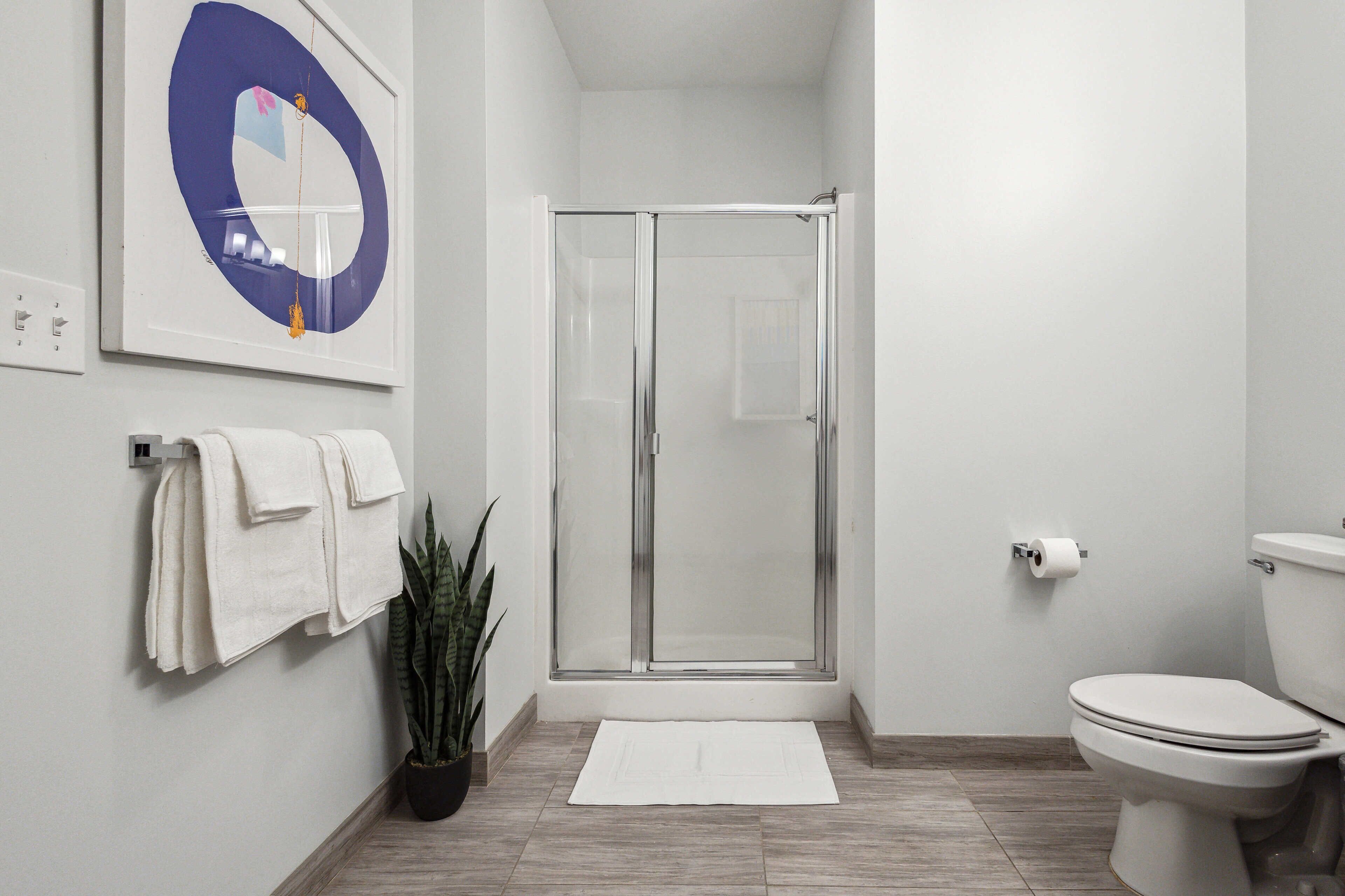 Un baño moderno con cabina de ducha de vidrio, inodoro y planta en maceta.