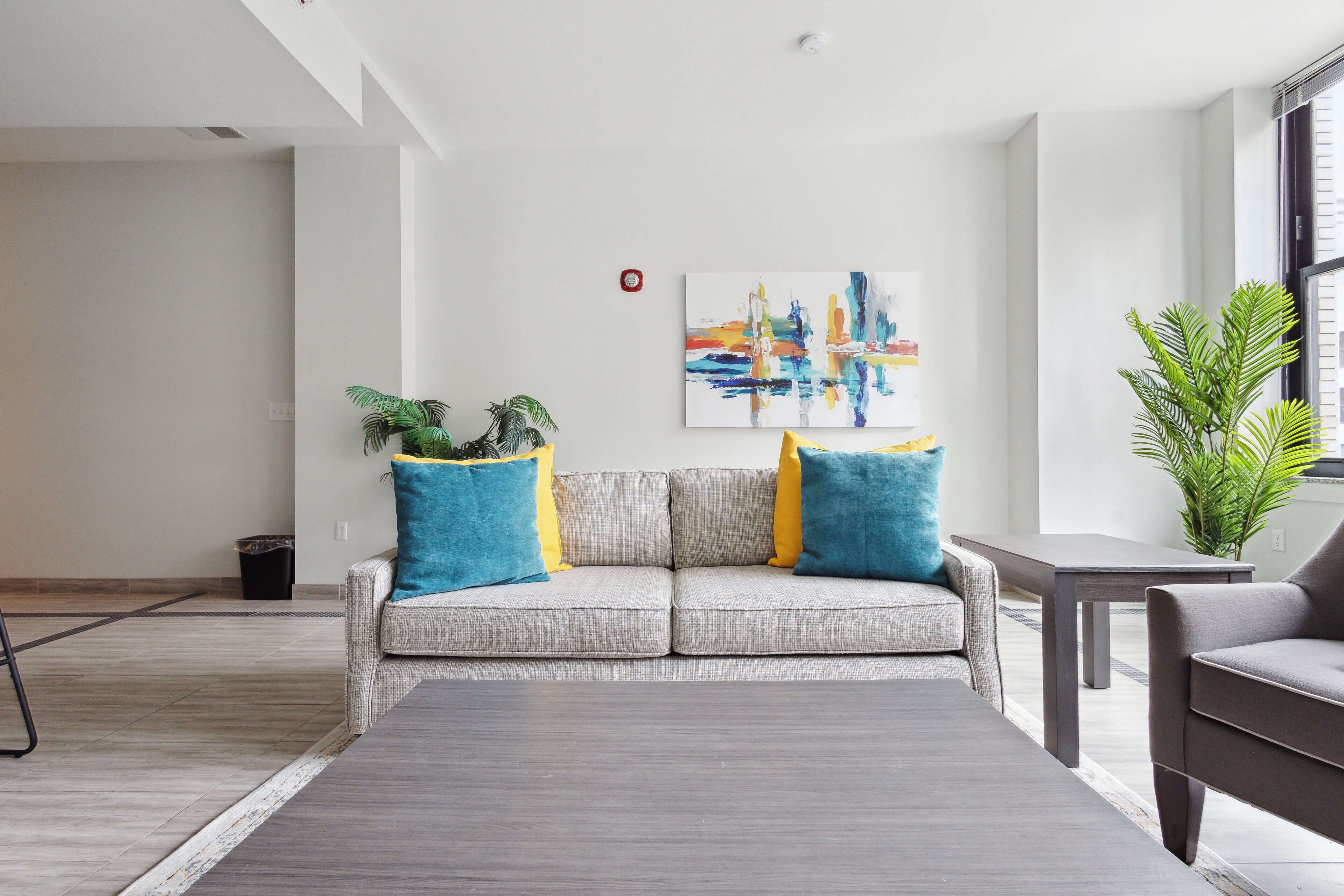 Una sala de estar moderna con un sofá gris, cojines azules y amarillos, una mesita de centro gris y una planta en maceta.