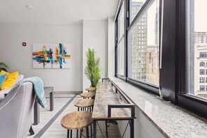 A modern living room with a long wooden table, a sofa, and a large window with a city view. - Executive Downtown Retreat (Detroit)