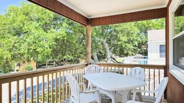 A covered outdoor patio with a table and four chairs, surrounded by wooden railings and overlooking a green landscape.