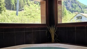 A spa area with a large bathtub, a view of a green landscape, and a decorative plant.