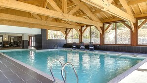 An indoor swimming pool with clear water, wooden beams, and a tiled floor.