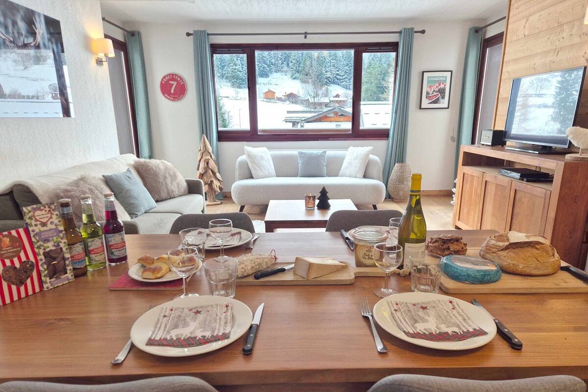 A cozy living room with a dining area set for a meal, featuring a sofa, a wooden table, and a television.