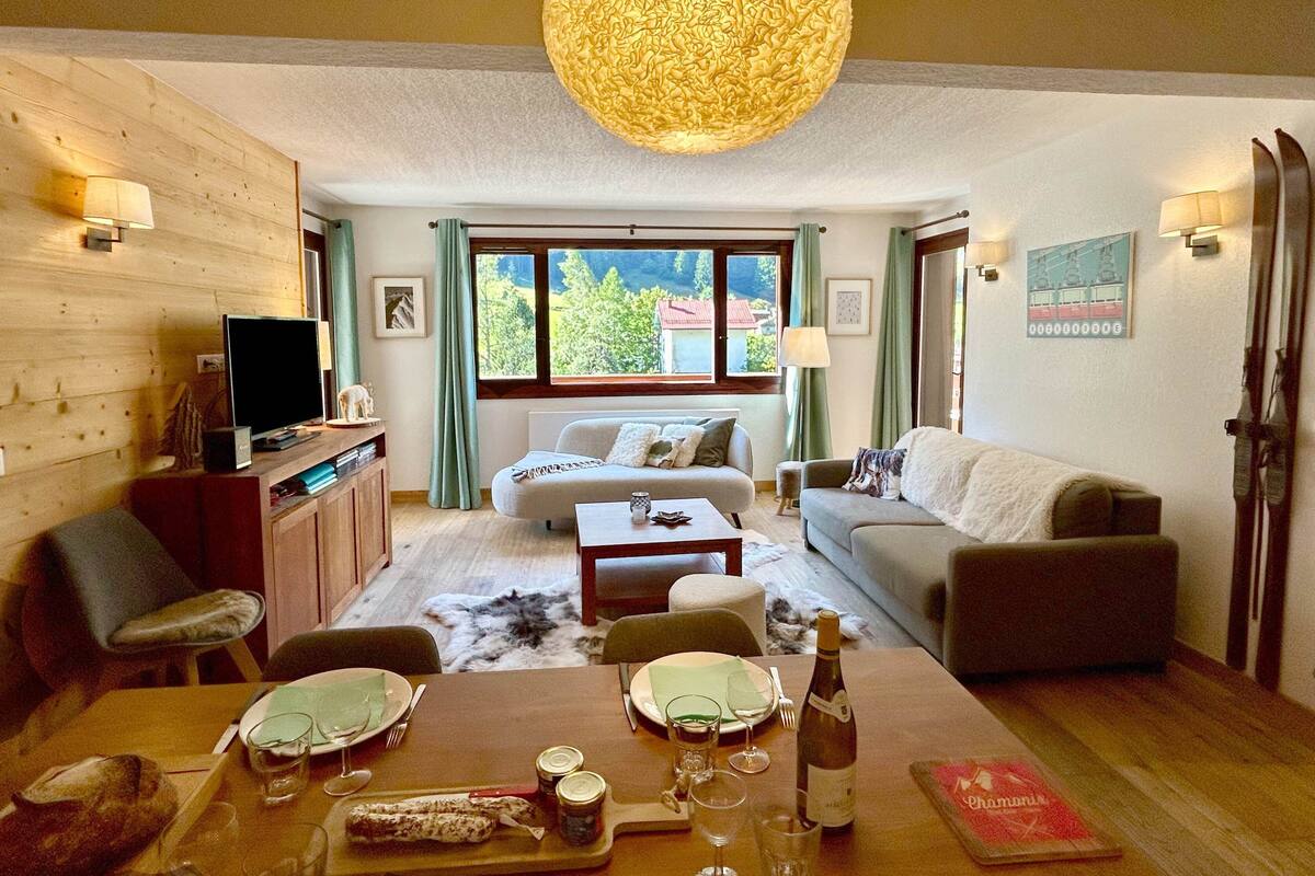 A cozy living room with a sofa, a dining table set for two, and a television on a wooden cabinet.
