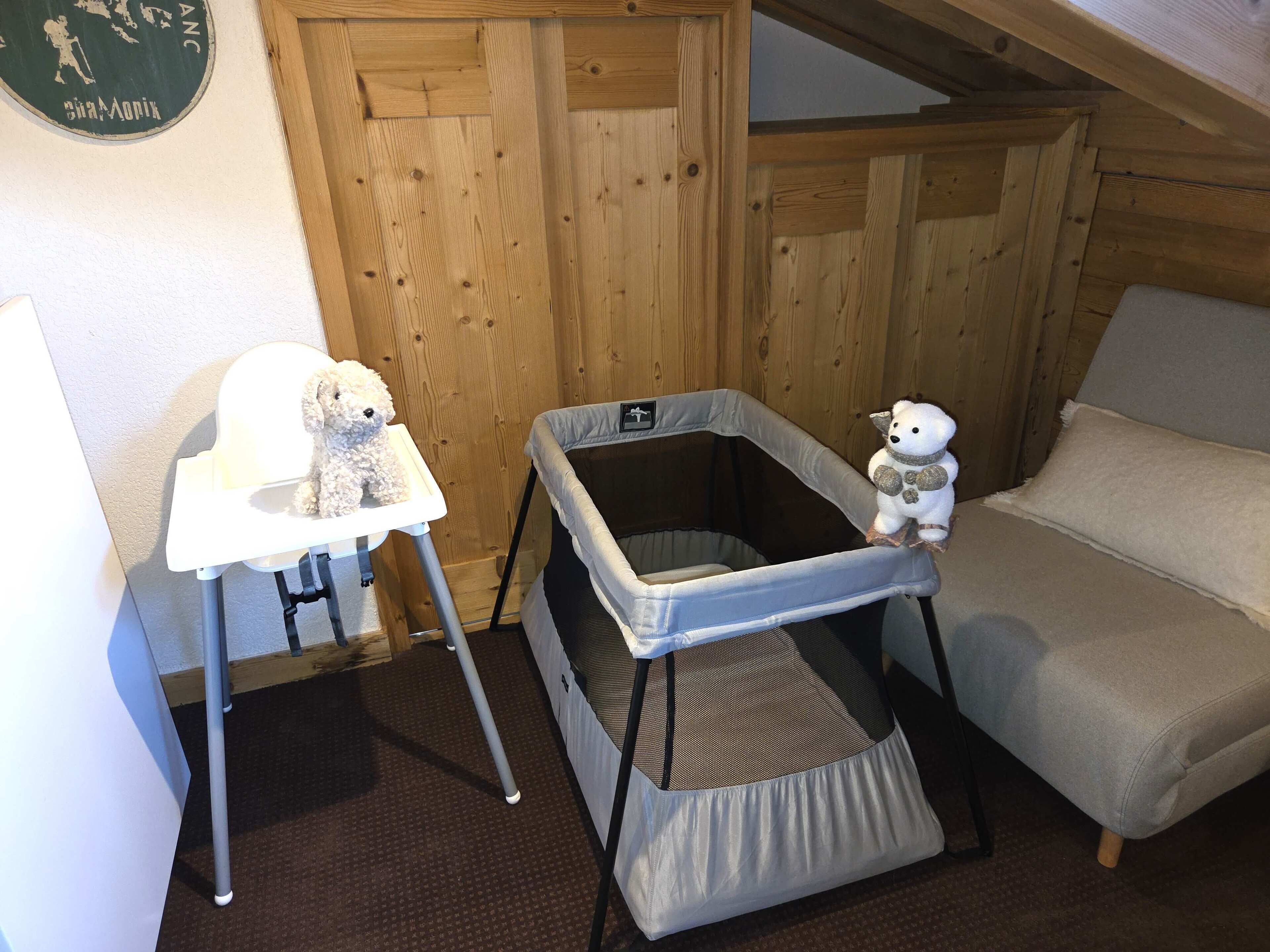 Een kamer met een houten wand, een witte stoel, een kleine hond, een babyren en een witte bank.
