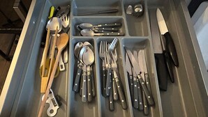 Eine Schublade mit Fächern, die verschiedene Küchenutensilien wie Löffel, Gabeln, Messer und eine Reibe enthalten.