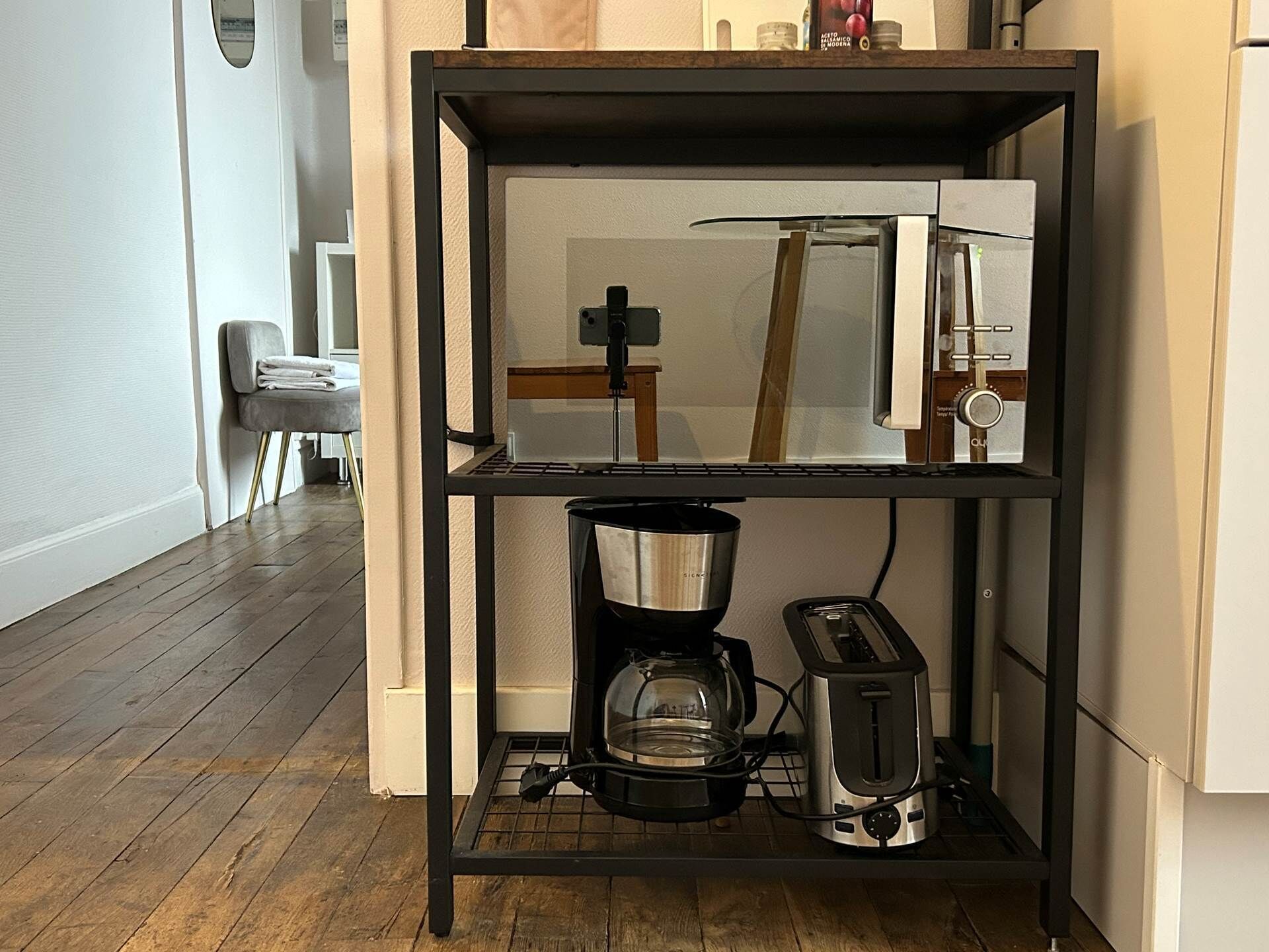 Une cuisine avec une étagère en métal noir qui contient une machine à café, un grille-pain et une bouilloire.