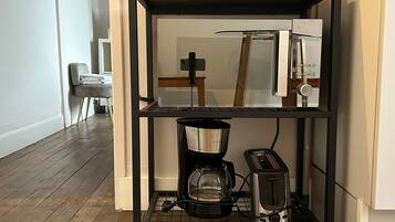 Une cuisine avec une étagère en métal noir qui contient une machine à café, un grille-pain et une bouilloire.