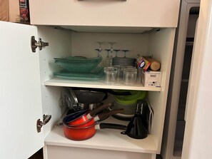 A kitchen cabinet with shelves holding glassware, a box of paper towels, and kitchen utensils. - Valletta (MARCILLAC LA CROISILLE)