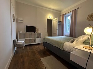 A bedroom with a bed, bedside table, lamp, TV, and a small seating area with a chair and cushions. - Valletta (MARCILLAC LA CROISILLE)