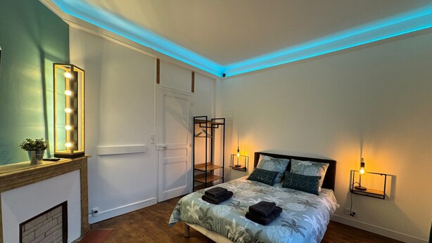 A bedroom with a bed, bedside lamps, a mirror with lights, a wardrobe, and a small table with a plant. - L'escale (Rennes)