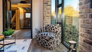Un coin accueillant avec un canapé à motifs, une petite table et une plante en pot. Un escalier mène à un étage supérieur, et une grande fenêtre offre une vue sur les arbres.