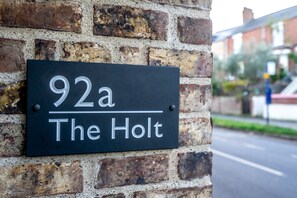 Un senyal negre amb lletra blanca sobre una paret de ma ó, que diu "92a The Holt".