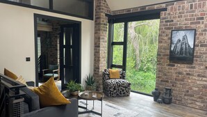 Un salon moderne avec un mur en briques, une grande fenêtre, un canapé, un fauteuil et une petite table.