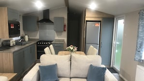 Een compact woongedeelte met een kitchenette, een bank met kussens en een eethoek.