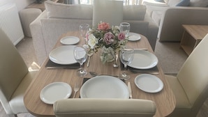 Een eettafel gedekt met borden, bestek en wijnglazen, omringd door banken en een decoratieve vaas.