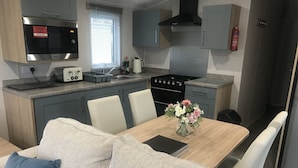 Een moderne keuken met een inbouwmagnetron, broodrooster en fornuis. Er is een eettafel met stoelen en een bloemenvaas.