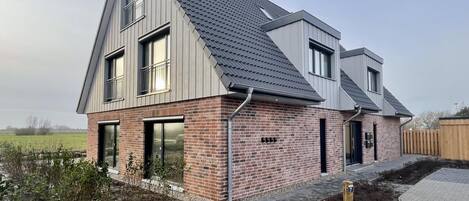Et moderne hus i to etager med skrå tag, murstensfacade og store vinduer.