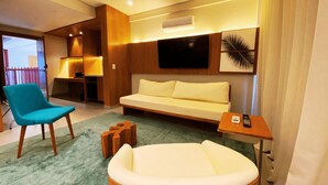 A modern hotel room with a sofa, a blue armchair, a small wooden table, and a round ottoman. - Flat Ilê de Pipa Samoa - By Almare (Tibau do Sul)