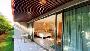 A modern bedroom with a large bed, a bedside table, and a window overlooking a garden. - Flat Ilê de Pipa Samoa - By Almare (Tibau do Sul)