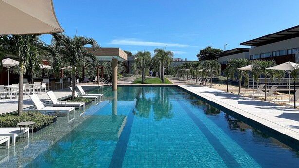 A swimming pool with lounge chairs and palm trees, surrounded by modern buildings. - Flat Ilê de Pipa Samoa - By Almare (Tibau do Sul)