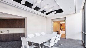 Et mødelokale med et langt bord, hvide stole og et moderne loftdesign.