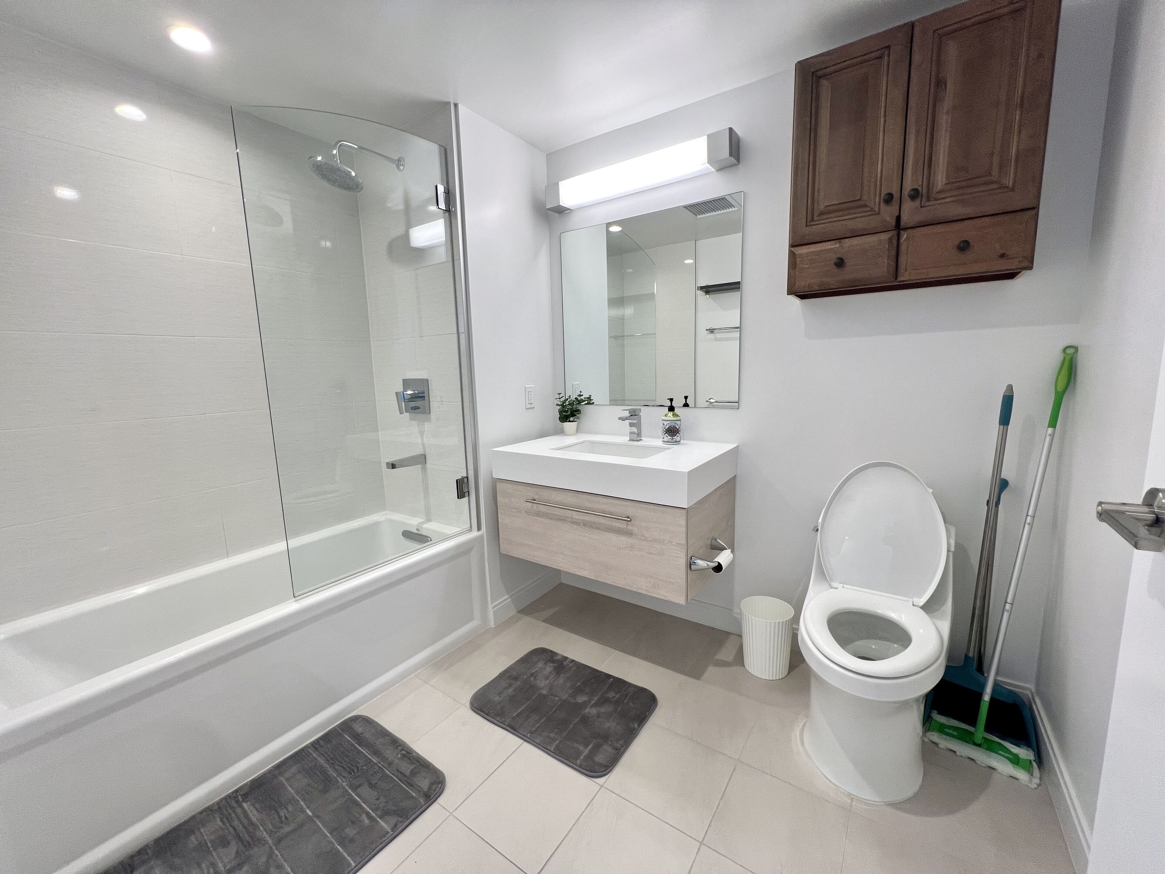A modern bathroom with a glass-enclosed shower, a white sink, a toilet, and a wooden cabinet above the mirror.
