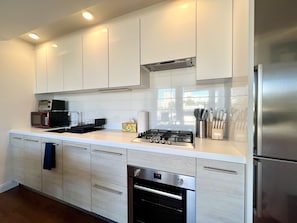 A modern kitchen with white cabinetry, stainless steel appliances, and a built-in oven.