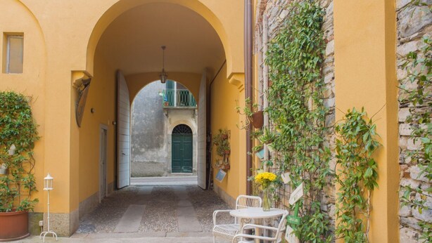 Une ruelle étroite avec un immeuble jaune, une porte verte et une table blanche entourée de chaises.