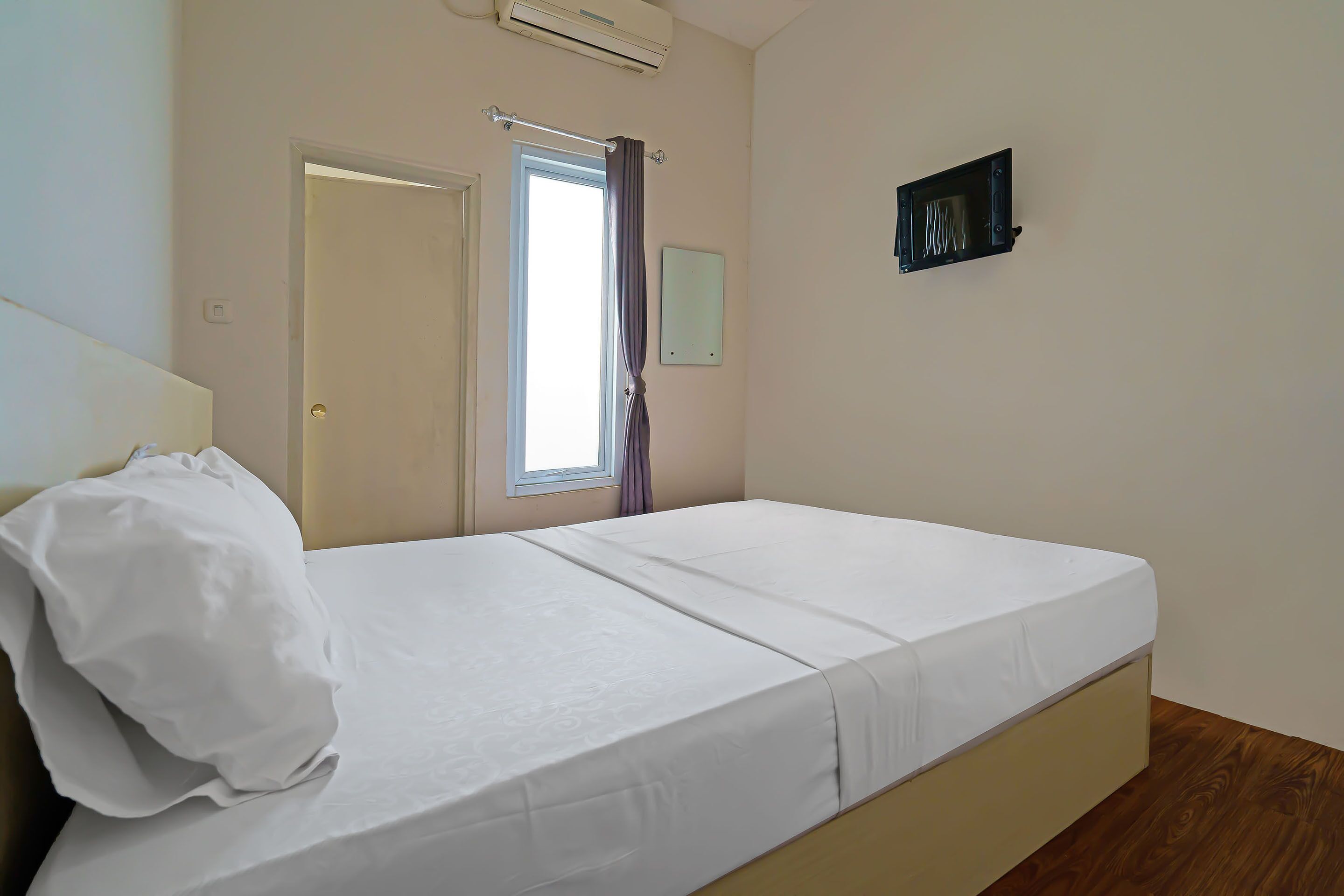 Een slaapkamer met een bed, een raam met gordijnen, een airconditioning en een lichtschakelaar aan de muur.