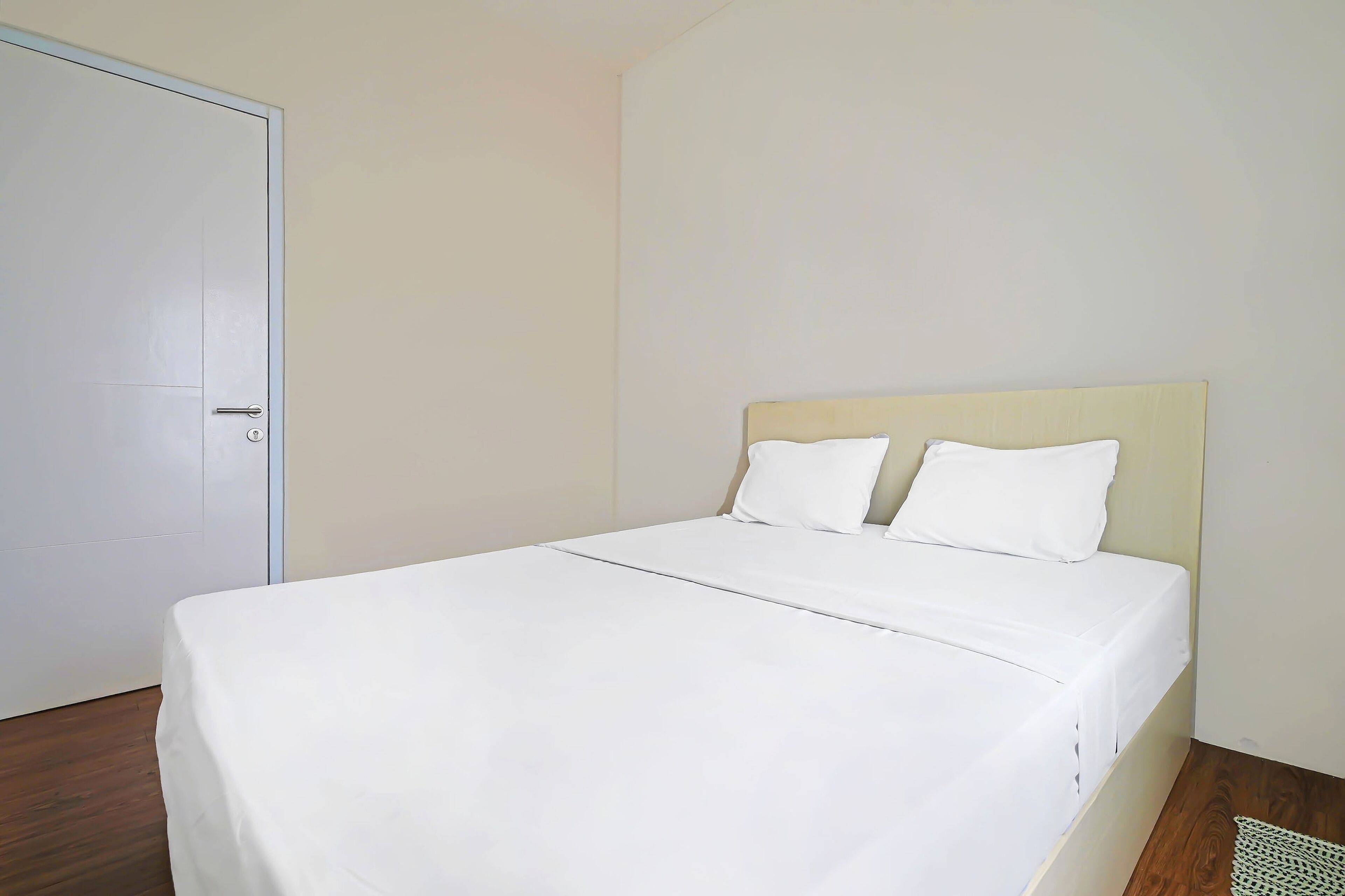 A single-bed room with a wooden floor, a white bedspread, and a plain wall.