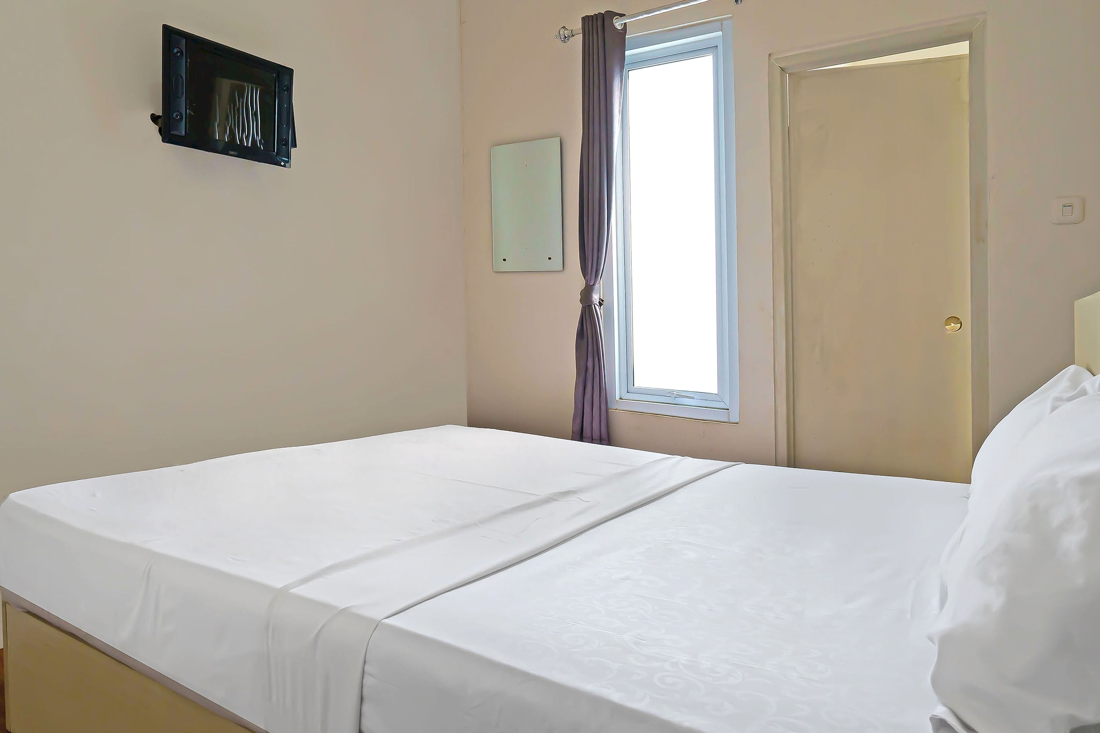 Una habitación sencilla y limpia con una cama, una ventana con cortinas, una puerta y un interruptor de luz en la pared.