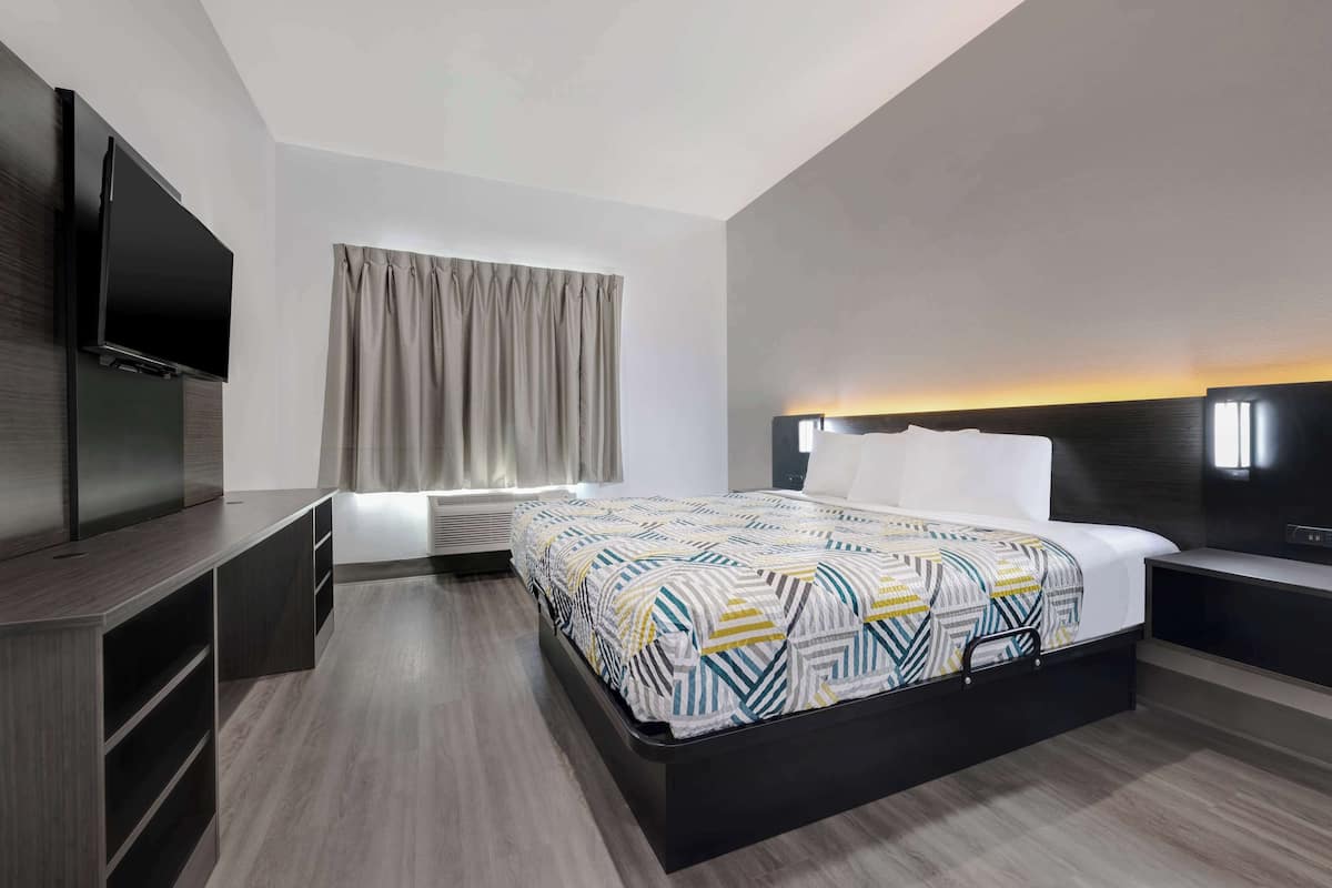 A modern hotel room with a large bed, built-in TV, and a bedside table.