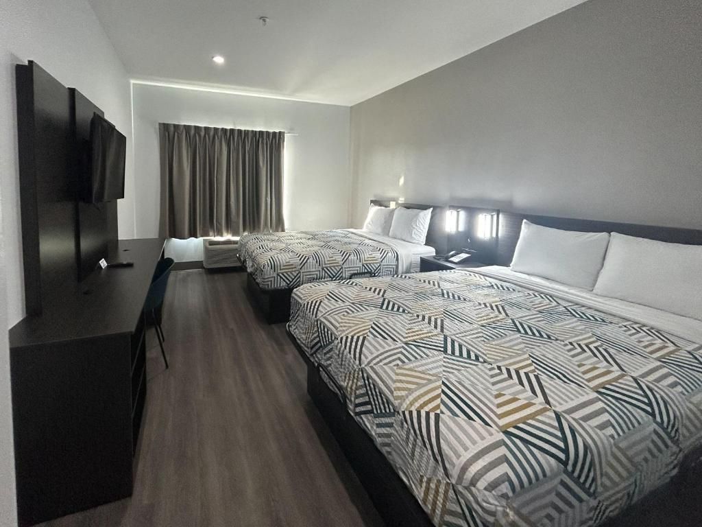 Habitación de hotel con dos camas, un escritorio, un televisor y una ventana con cortinas.