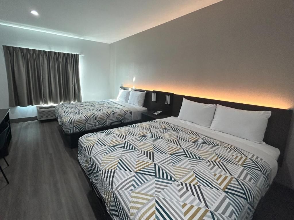 Una habitación de hotel con dos camas, un escritorio y un ventanal con cortinas.