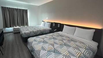 Una habitación de hotel con dos camas, un escritorio y un ventanal con cortinas.