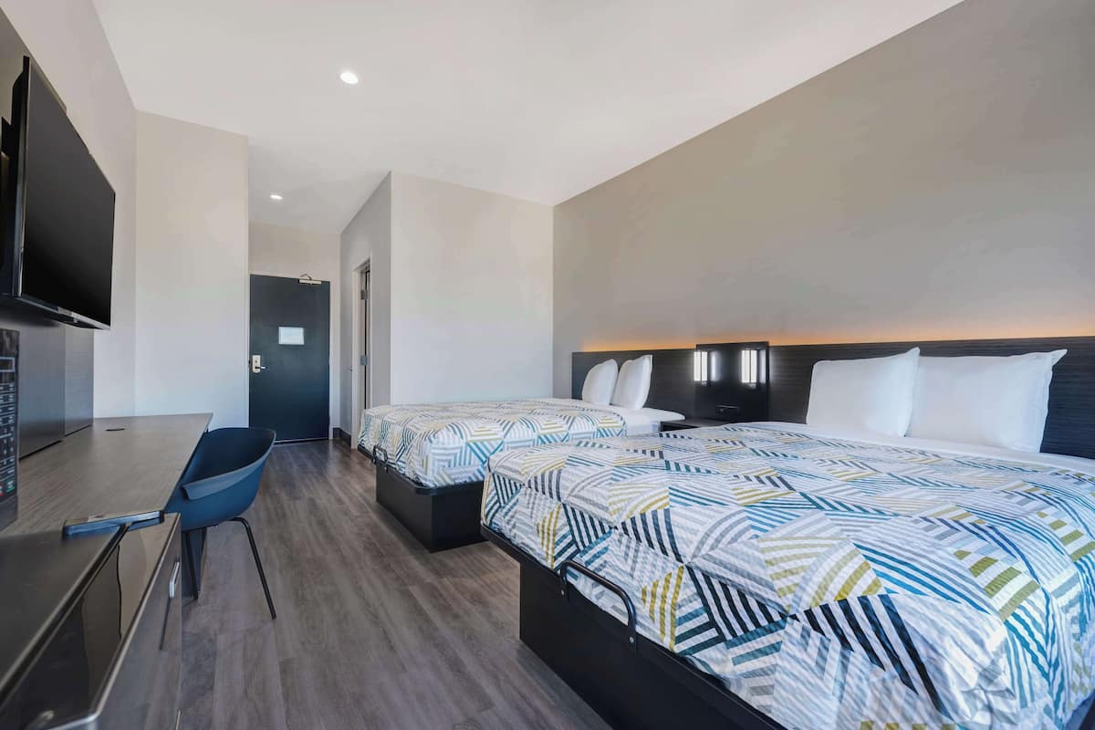 A hotel room with two beds, a desk, a chair, and a TV.