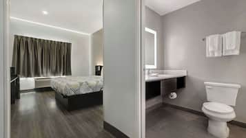 Habitación de hotel moderna con cama, mesita de noche y baño equipado con inodoro, lavabo y toallero.