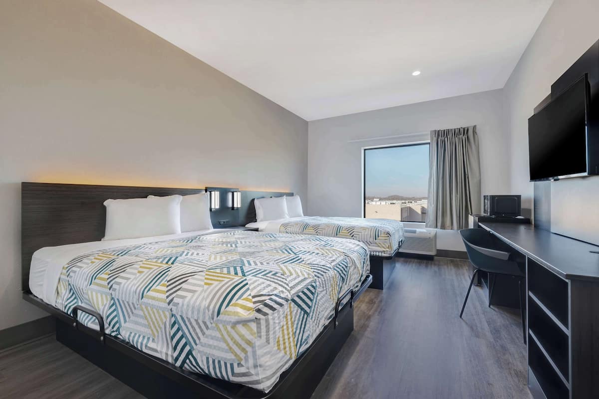 A hotel room with two beds, a desk, a TV, and a large window with a view.