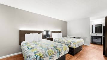 A hotel room with two beds, a desk, a chair, a mirror, and a small kitchenette.